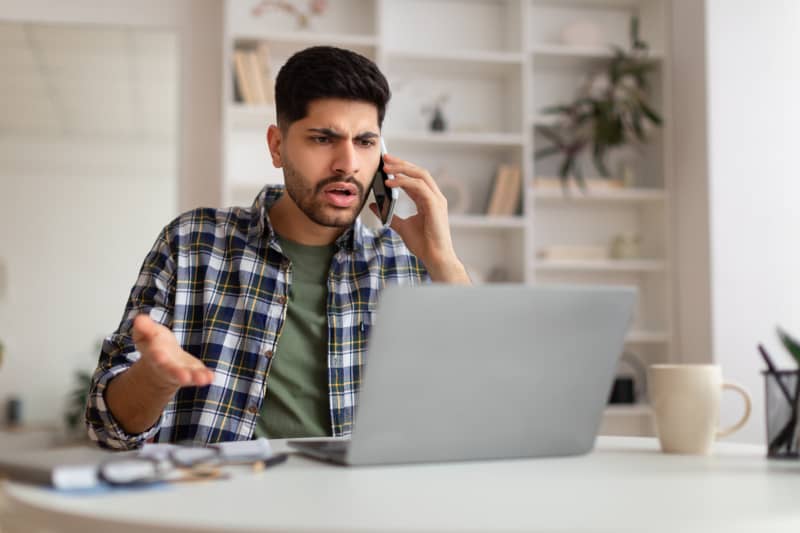 hombre discutiendo por teléfono frente a su computadora